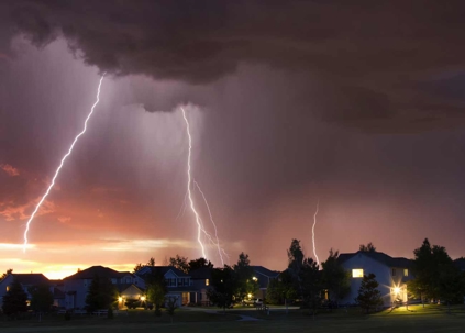 lightning striking in the background over a neighborhood